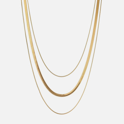 Three gold-toned chains of different widths hanging in layers against a plain light background 1