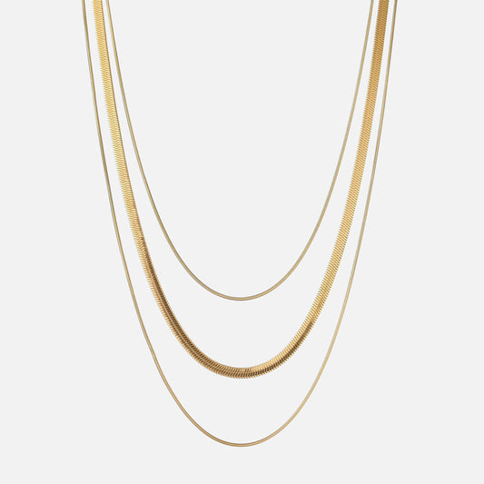 Three gold-toned chains of different widths hanging in layers against a plain light background 1