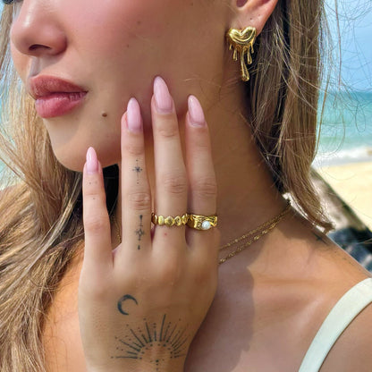 Close-up of a woman on a beach wearing a gold dripping heart earring and rings 4