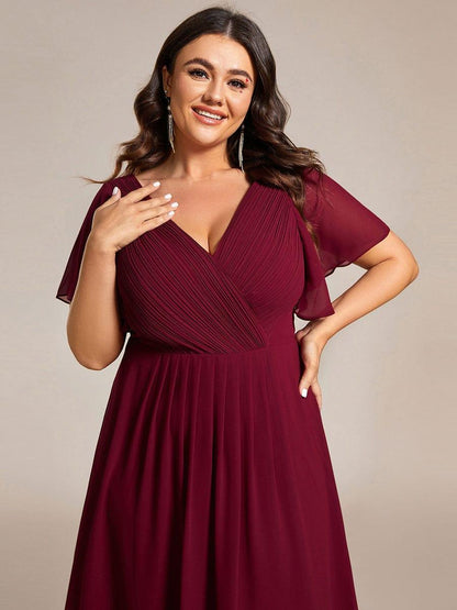 Close-up of the burgundy pleated wrap bodice and flutter sleeves on a smiling plus-size model. 51