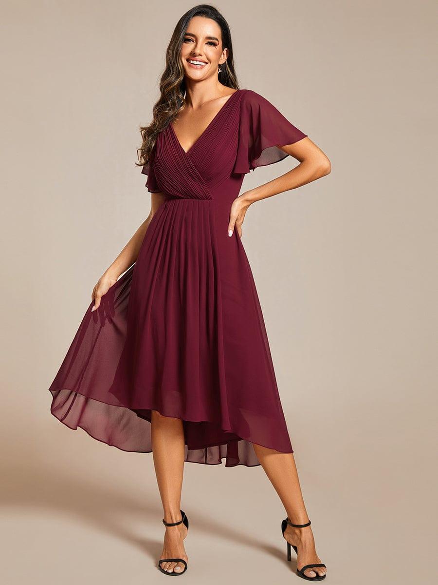 Model in burgundy high-low chiffon dress with black heels, smiling and lifting one side of the skirt. 48