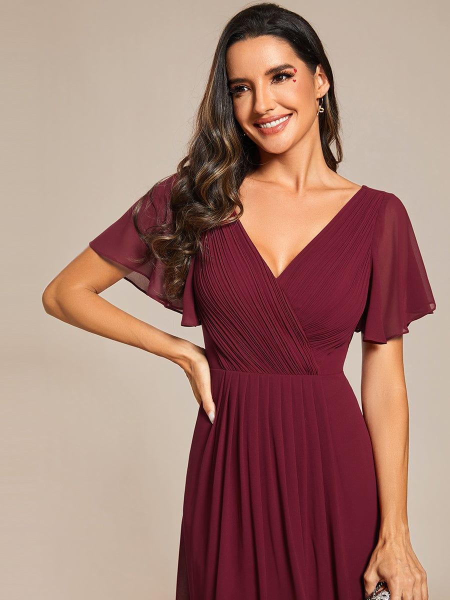 Close-up of a burgundy pleated V-neck bodice with sheer flutter sleeves, worn by a smiling model with hand on hip. 46