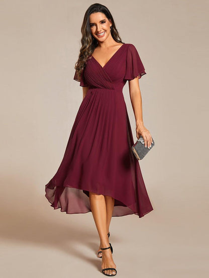 Front view of the burgundy chiffon dress on a model, with pleated wrap bodice, high-low hem and a sparkly clutch. 3