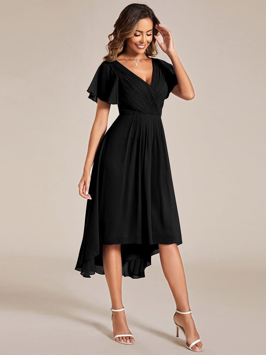 Black high-low chiffon dress on a model with one hand raised to her hair, seen from a three-quarter angle. 25