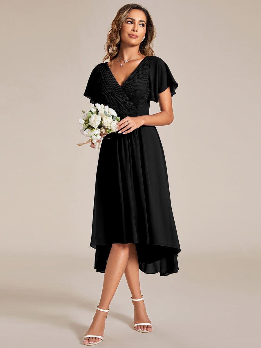 Model in the black dress holding a small bouquet of white flowers, wearing white strappy heels. 24