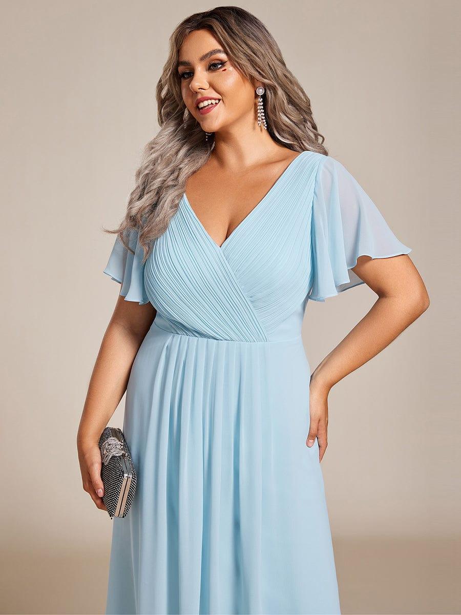 Close-up of the light blue dress's pleated wrap bodice and flutter sleeves on a plus-size model holding a clutch. 91