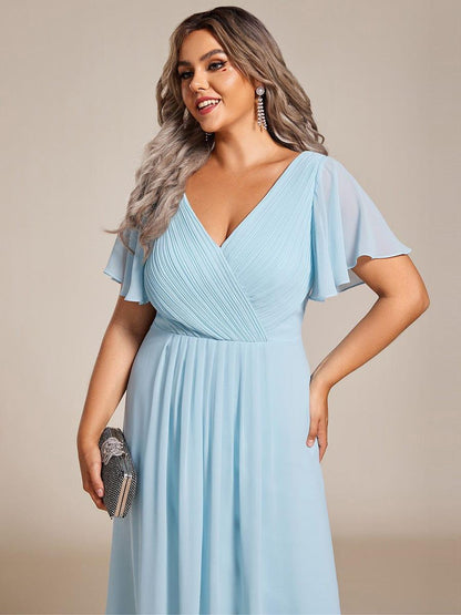 Close-up of the light blue dress's pleated wrap bodice and flutter sleeves on a plus-size model holding a clutch. 91