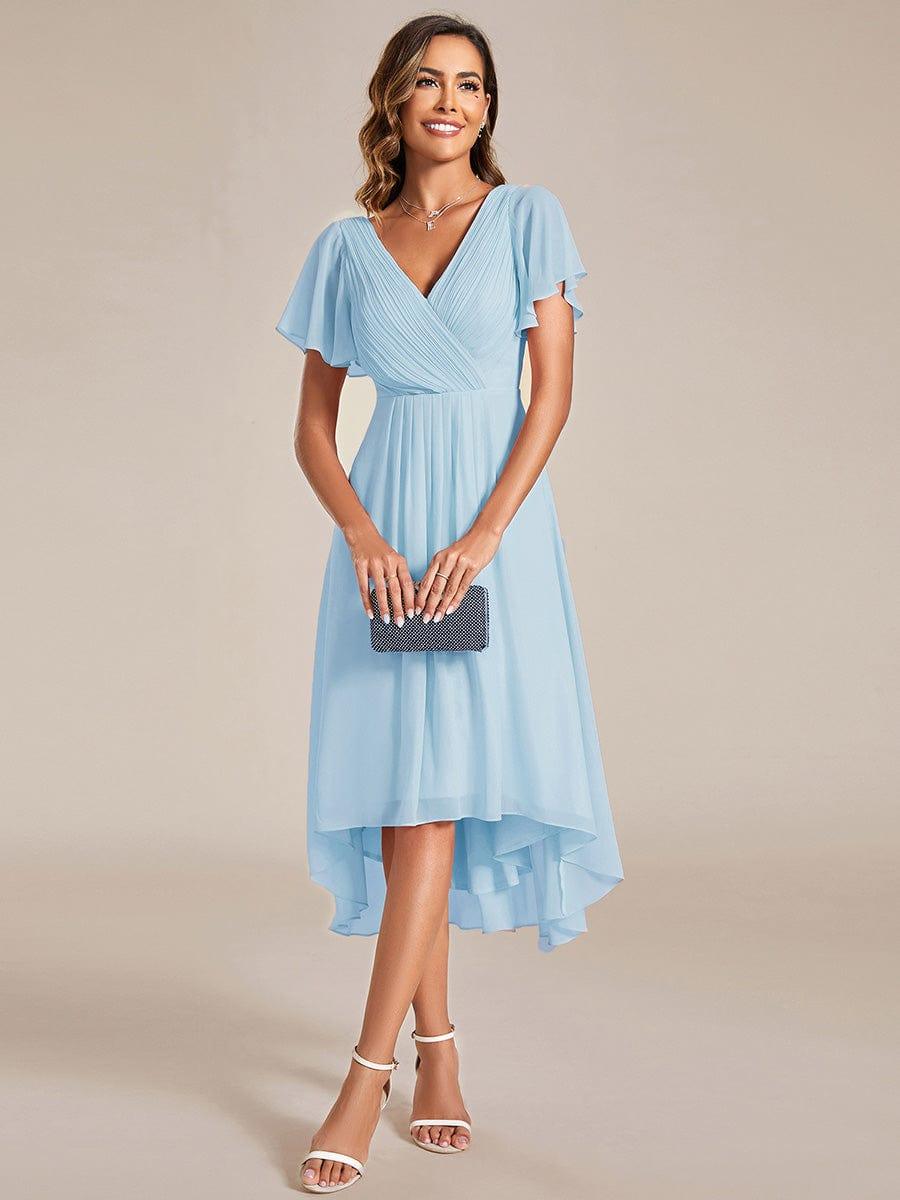 Model in the light blue dress holding a small sparkly clutch, standing front-on with white heels. 87