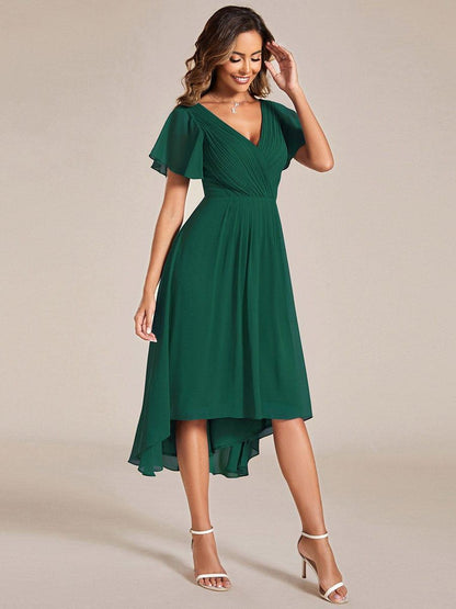 Three-quarter view of the dark green dress, model smiling with a hand raised to her hair, showing the high-low hem. 14