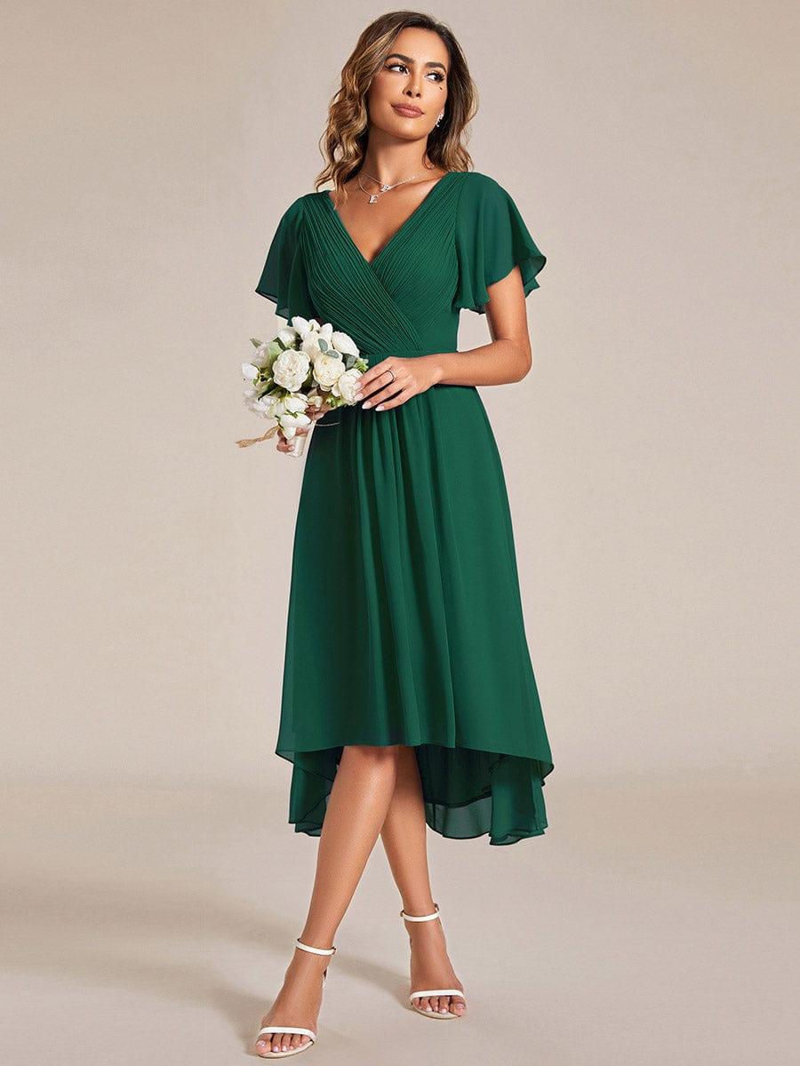 Model in the dark green dress holding a small white flower bouquet, looking to the side, full-length front view. 13