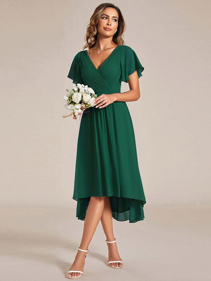Model in the dark green dress holding a small white flower bouquet, looking to the side, full-length front view. 13
