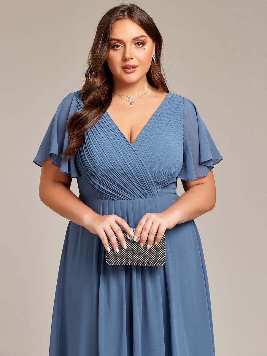 Close-up of the dusty blue pleated wrap bodice and flutter sleeves, with the model holding a black sparkly clutch. 43