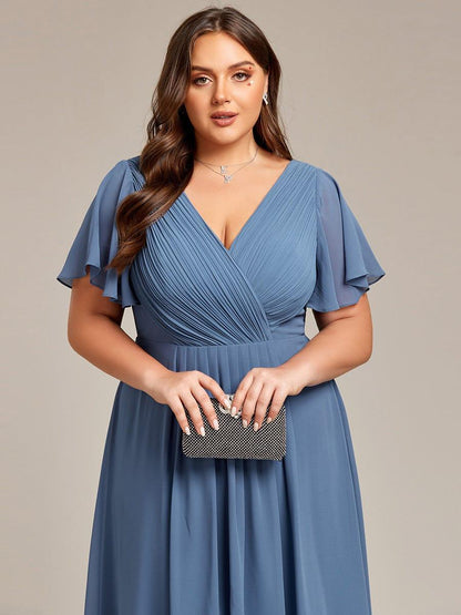 Close-up of the dusty blue pleated wrap bodice and flutter sleeves, with the model holding a black sparkly clutch. 43