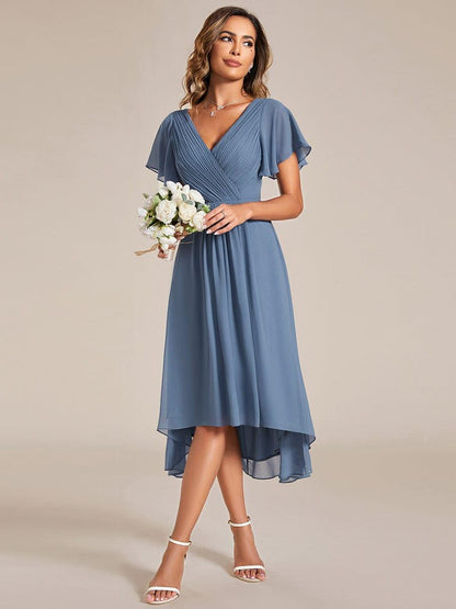 Model in the dusty blue dress holding a small bouquet of white flowers, showing the full high-low skirt. 8