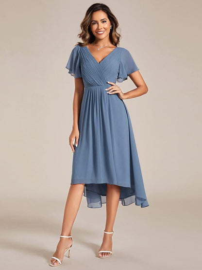 Dusty blue version of the dress on a model with one hand on hip, front view, worn with white heeled sandals. 5