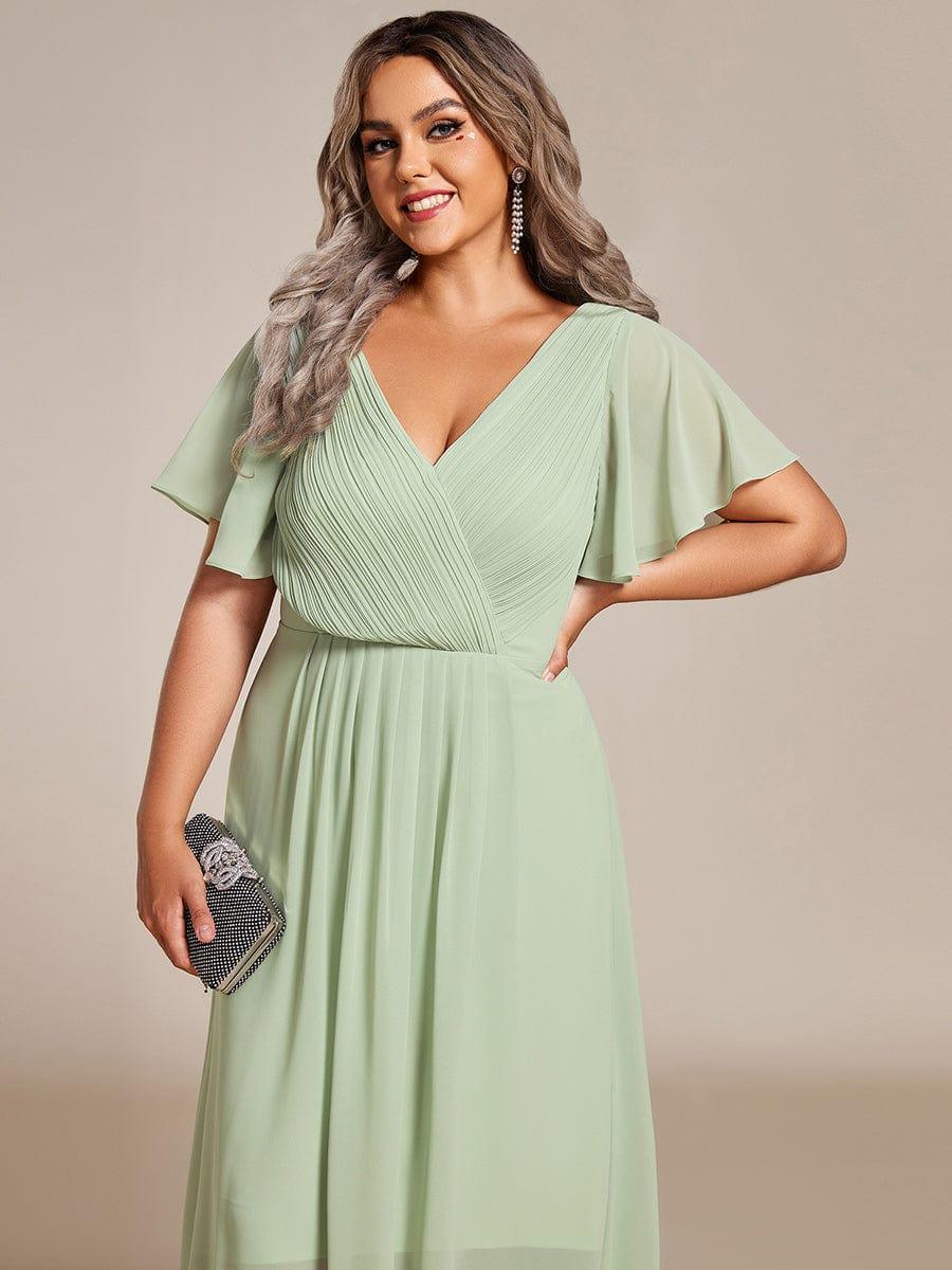 Close-up of the mint green dress's pleated wrap bodice and flutter sleeves, with a sparkly clutch held at the side. 83
