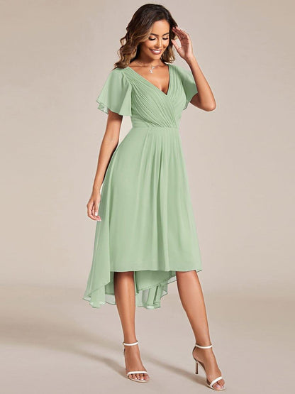 Model in the sage green dress with a hand raised to her hair, showing the high-low hem. 80