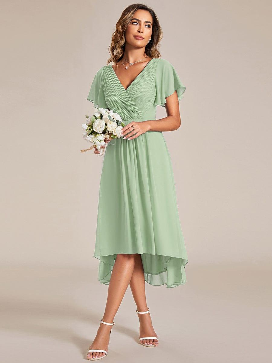 Model in the sage green dress holding a small bouquet of white flowers, looking to the side. 79