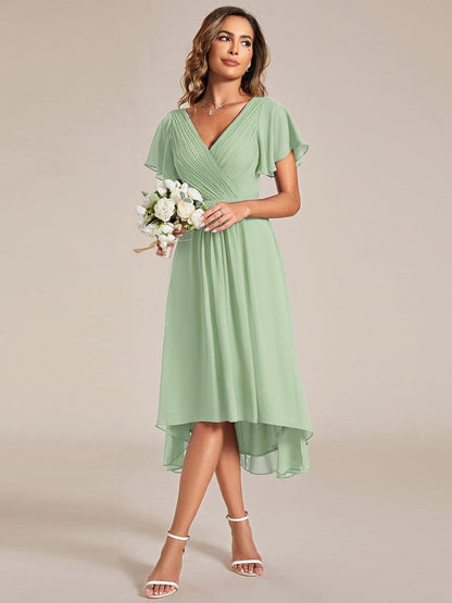 Model in the sage green dress holding a small bouquet of white flowers, looking to the side. 79