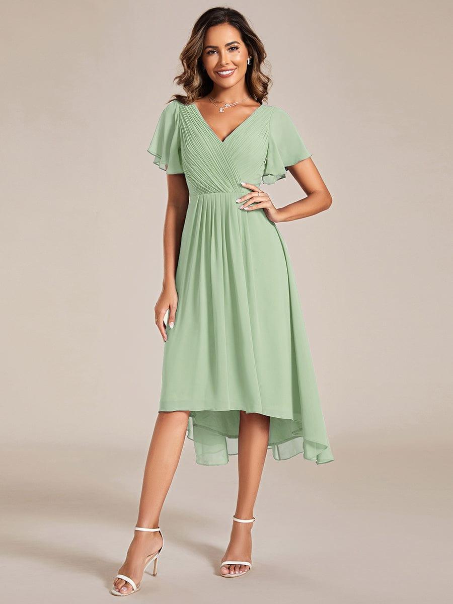 Model in the pale sage green version of the dress, front view with white heeled sandals. 76
