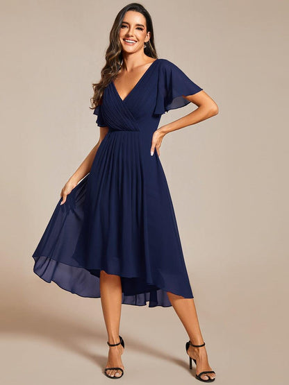 Model in navy high-low chiffon dress with black heels, smiling and lifting one side of the skirt. 54