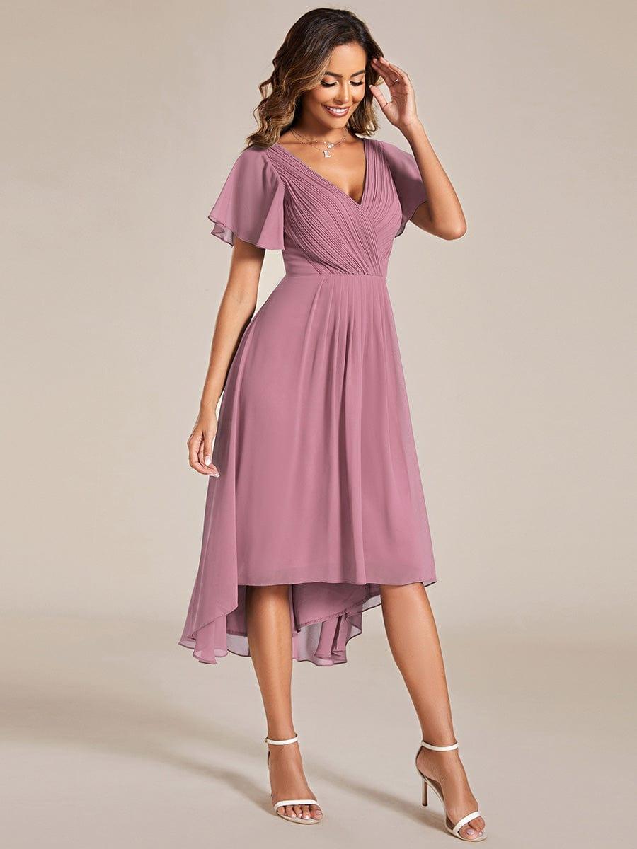 Model in the dusky pink dress with a hand raised to her hair, showing the high-low hem. 62