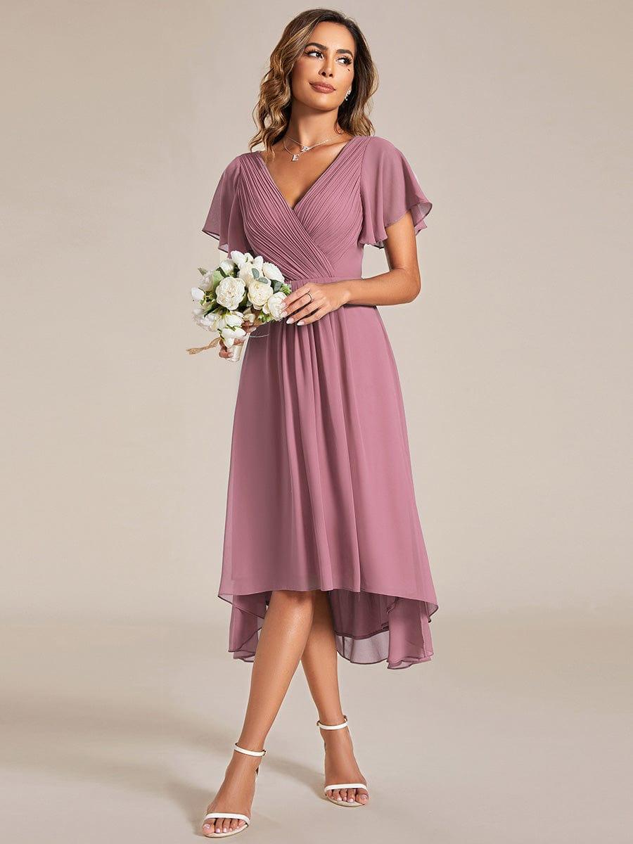 Model in dusty rose pink high-low chiffon dress holding a bouquet of white flowers, with white heeled sandals. 60