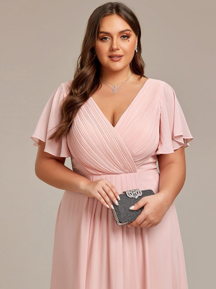 Close-up of the pale pink dress's pleated V-neck bodice and flutter sleeves, with a sparkly clutch held in front. 33