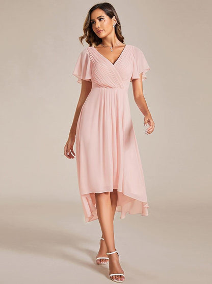 Walking pose in the pink dress, showing the pleated V-neck bodice, flutter sleeves and flowing high-low skirt with white sandals. 20