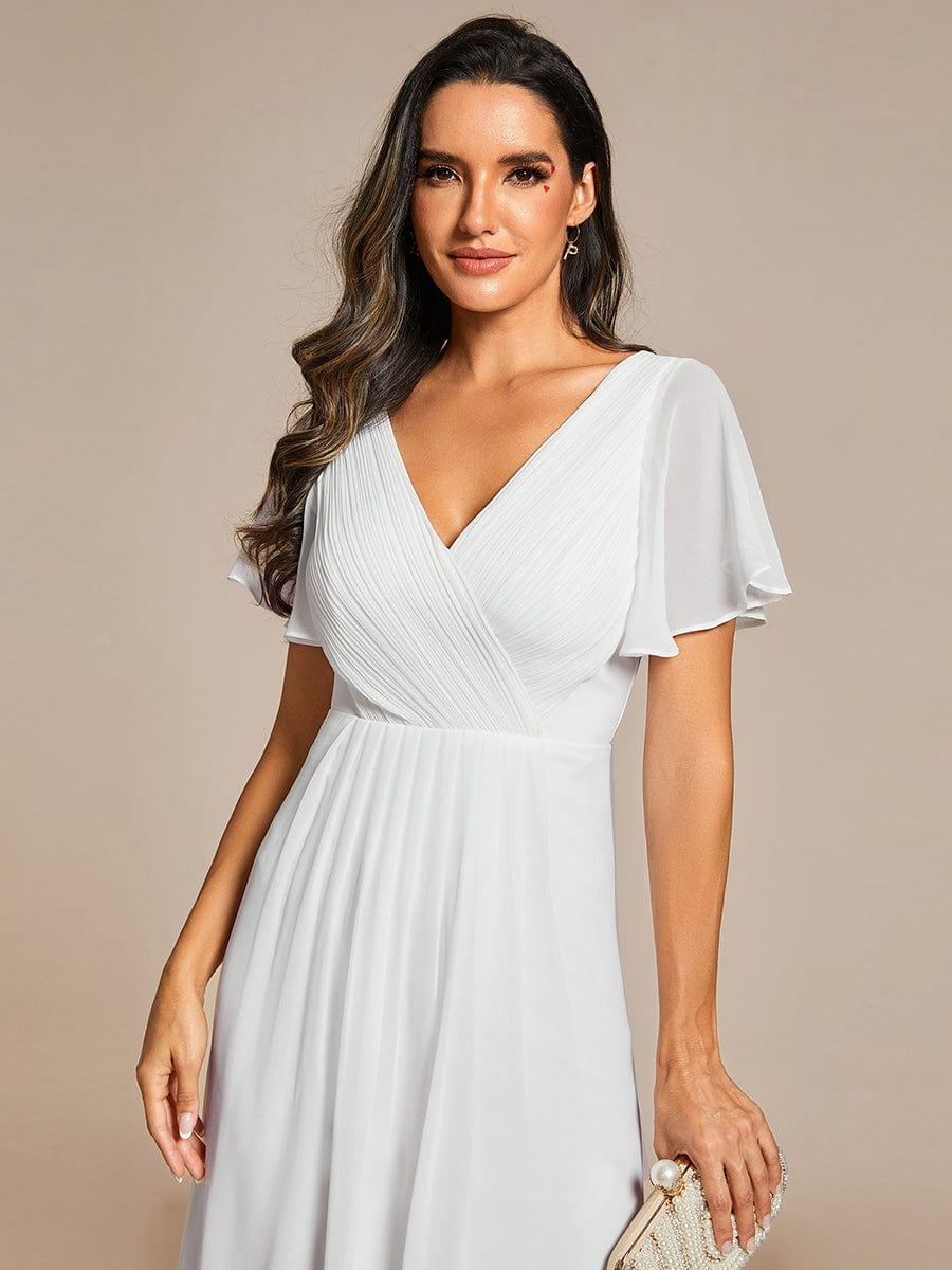 Close-up of the white dress's pleated wrap V-neckline and sheer flutter sleeves, with a pearl clutch. 70
