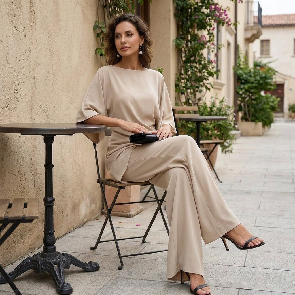 Model seated at a café table in the beige set, legs crossed, with a black clutch resting on her lap. 12