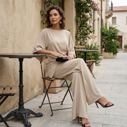 Model seated at a café table in the beige set, legs crossed, with a black clutch resting on her lap. 12