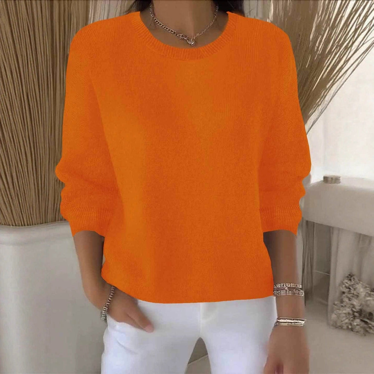 Woman wearing a bright orange round-neck knit jumper with ribbed cuffs and white trousers 11