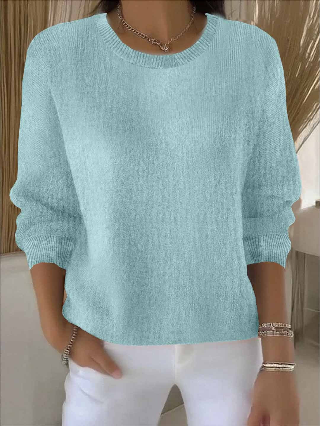 Woman wearing a pale aqua round-neck knit jumper with ribbed neckline, with white trousers 10