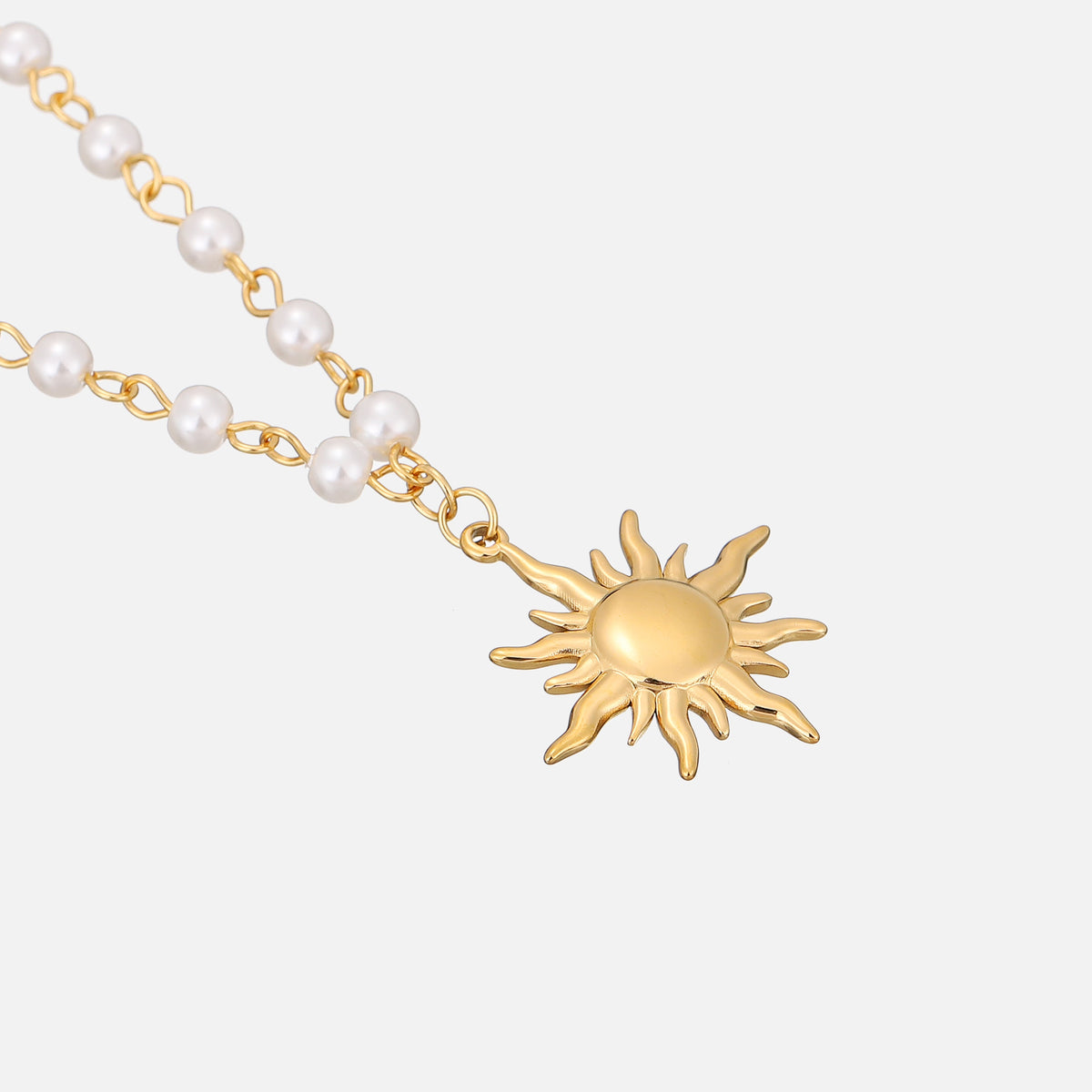 Angled close-up of the wavy-rayed gold sun pendant and pearl links lying on a pale surface 2