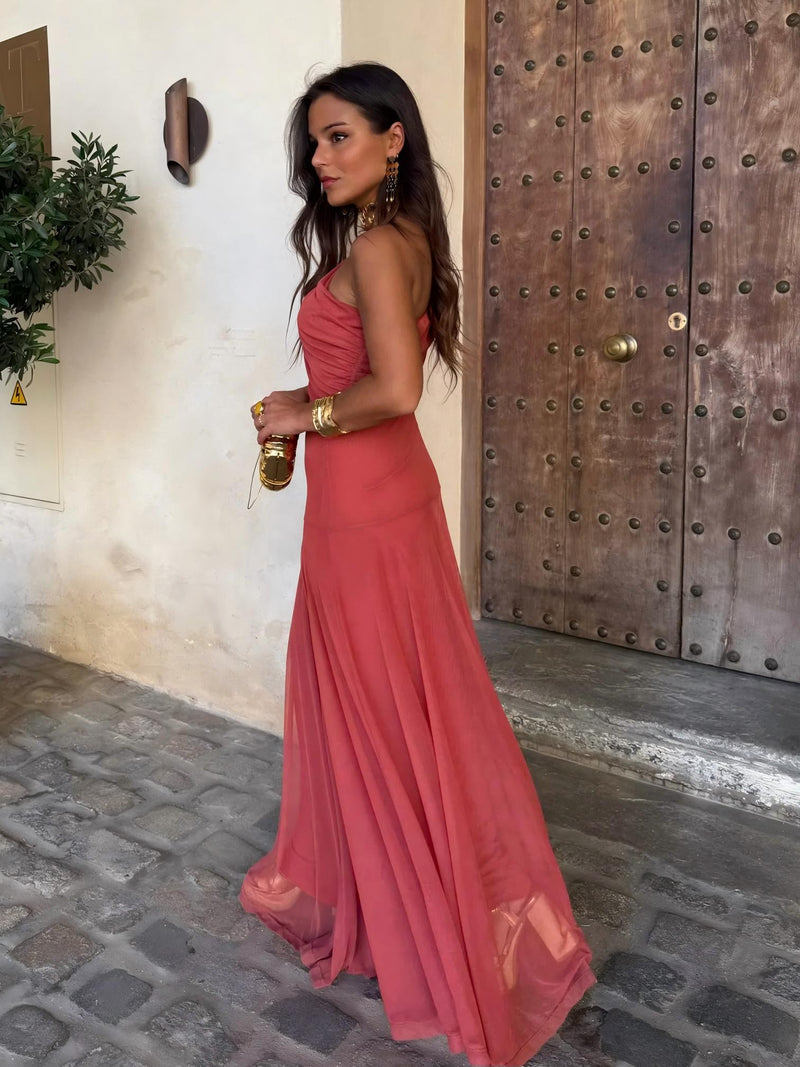 Side view of terracotta one-shoulder maxi dress with a long flowing skirt, holding a small gold bag 5