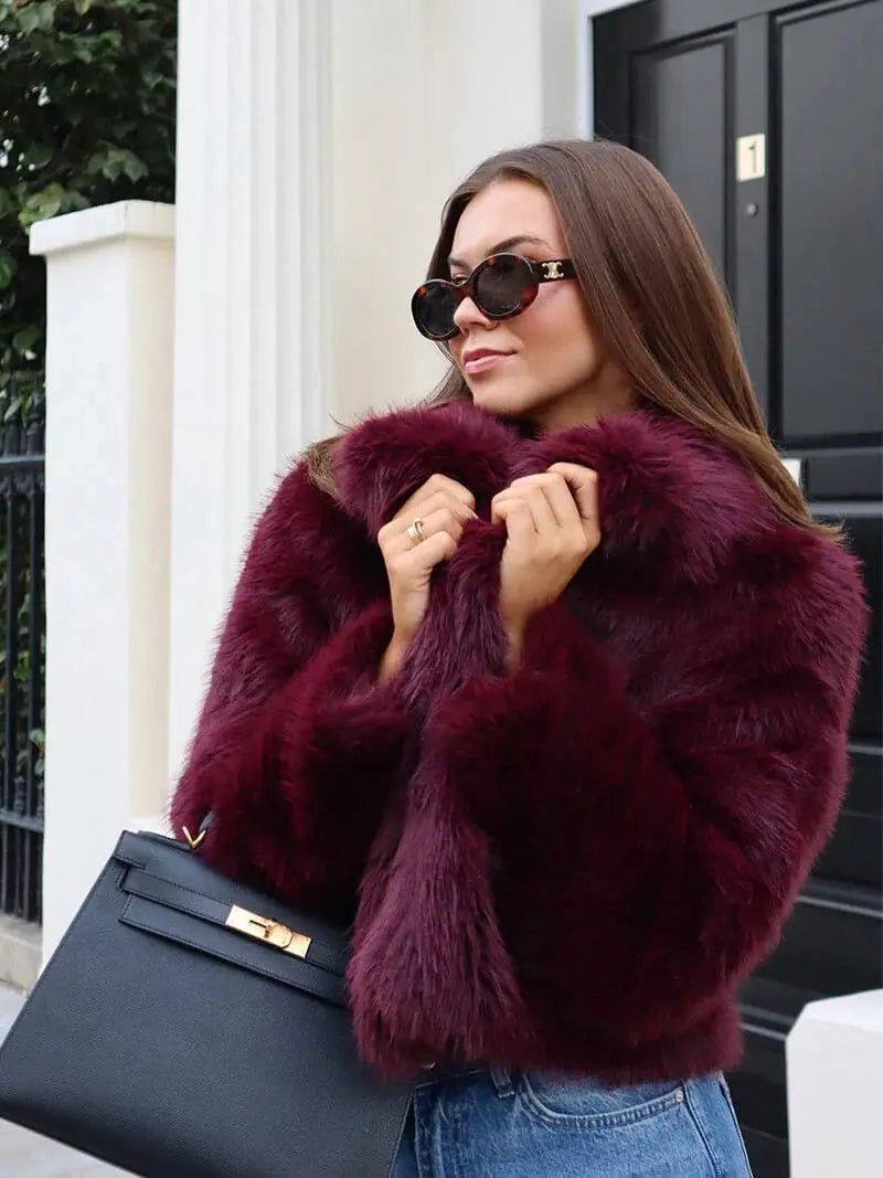 Close-up of a woman in sunglasses gripping the lapels of a burgundy faux fur coat 13