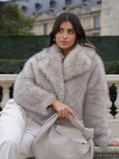 Woman wearing a light grey faux fur coat with a big collar, holding a woven bag 6
