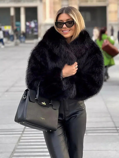 Smiling woman in sunglasses wearing a black faux fur coat with leather-look trousers and a black handbag 7