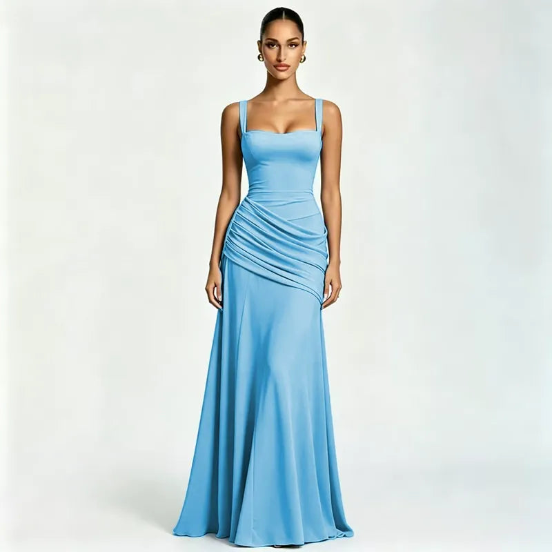 Model in a sky blue maxi dress with square neckline, wide straps and ruched waist, against a plain pale studio backdrop. 21