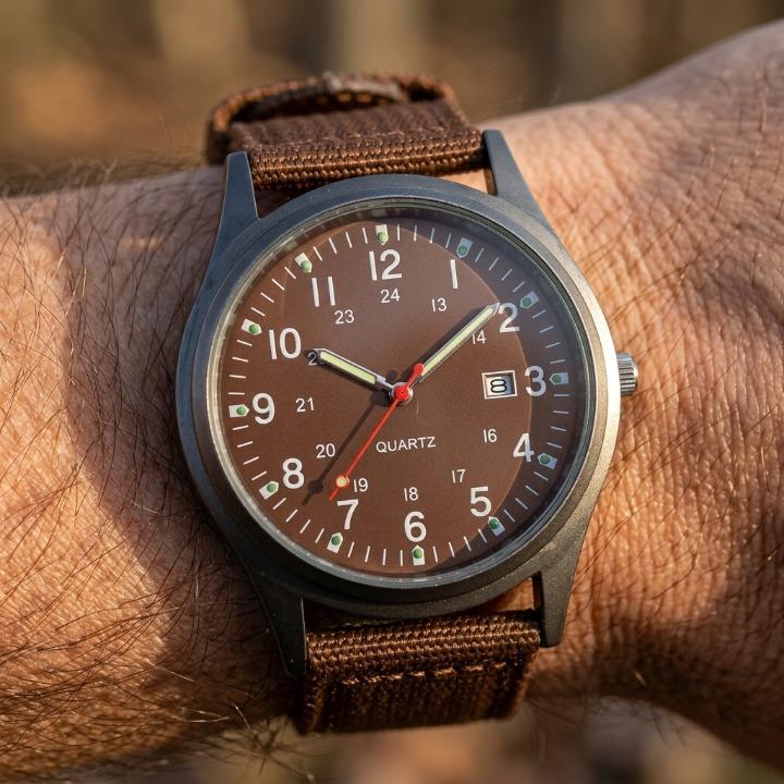 Close-up of the brown-dialled watch with brown nylon strap on a wrist, showing luminous hands and the date window. 4