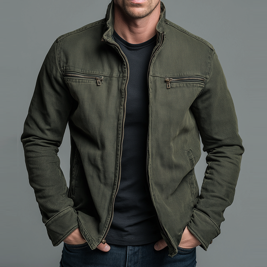 Man wearing an olive green zip-up jacket with chest zip pockets over a black T-shirt, hands in pockets, front view. 1