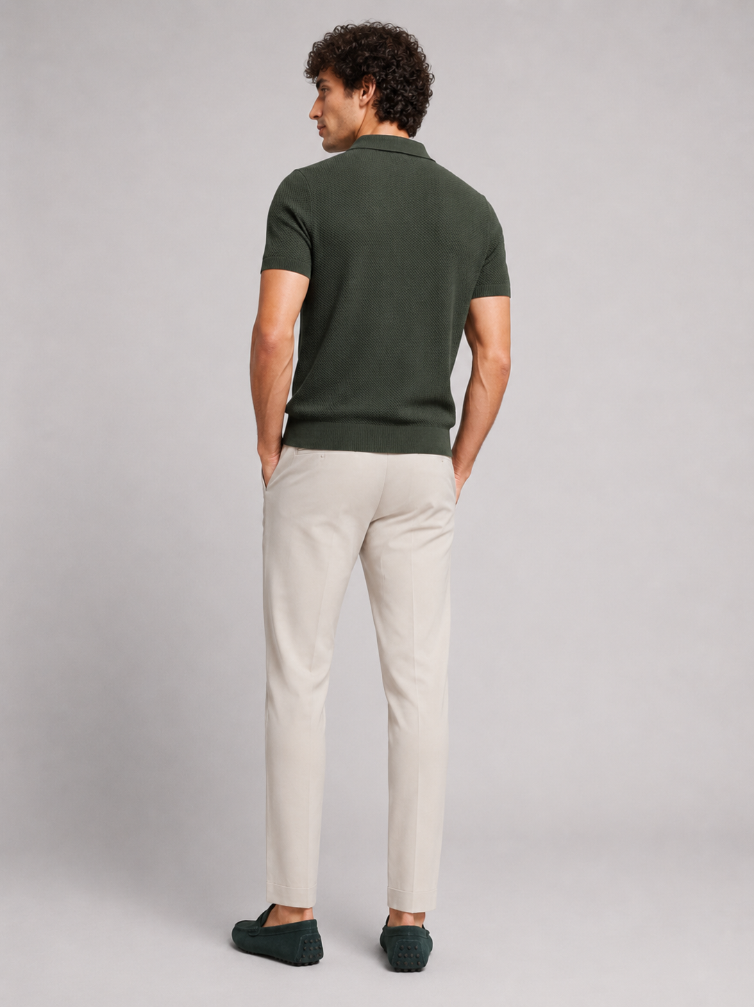Back view of model wearing dark green knit polo with beige trousers and green driving loafers 14