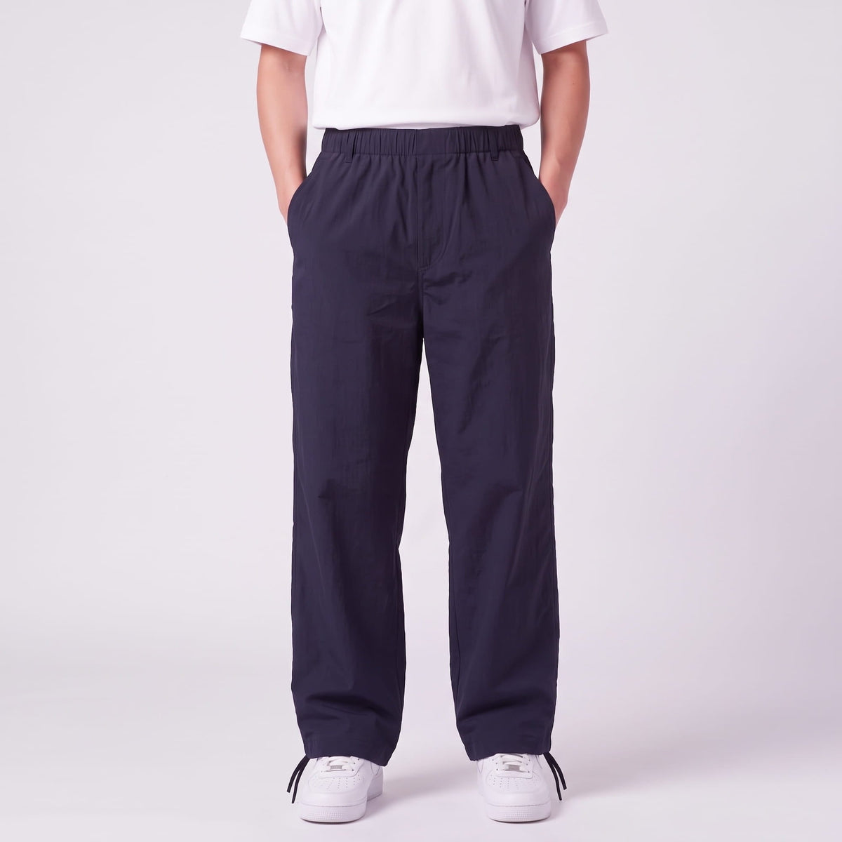 Front view of navy wide-leg trousers with elasticated waist and side pockets, worn by a model with hands in pockets. 1
