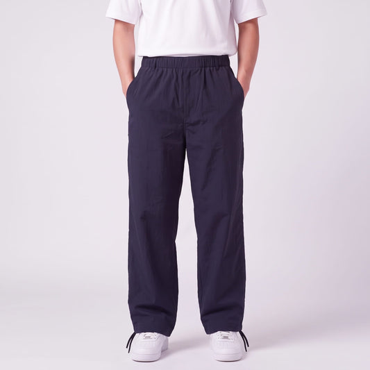Front view of navy wide-leg trousers with elasticated waist and side pockets, worn by a model with hands in pockets. 1