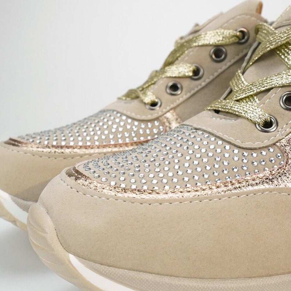 Close-up of the toe of beige trainers, showing the sparkly studded panel, gold laces, metal eyelets and rose-gold edging. 10
