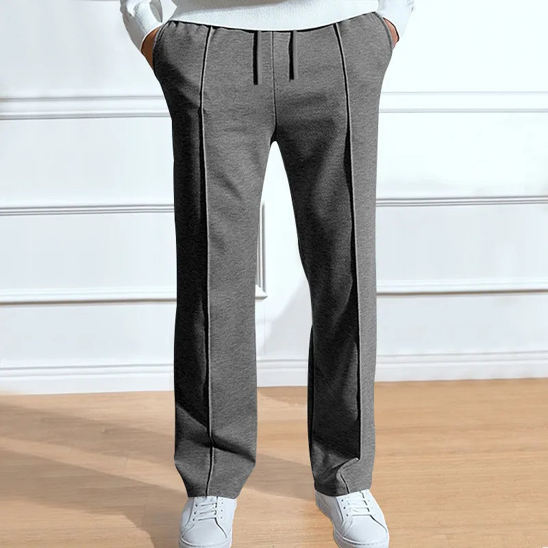 Front view of the trousers in marl grey on a model, with centre creases, drawstring waist and white trainers. 2