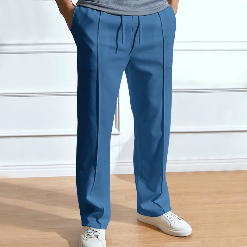 Model wearing the trousers in mid blue, front view with drawstring waist and creased legs, paired with white trainers. 5