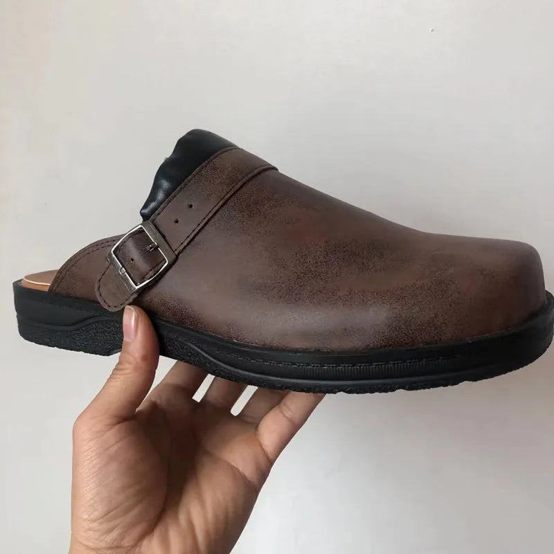 Dark brown clog with a silver buckle strap and black sole, held in one hand against a plain wall. 2