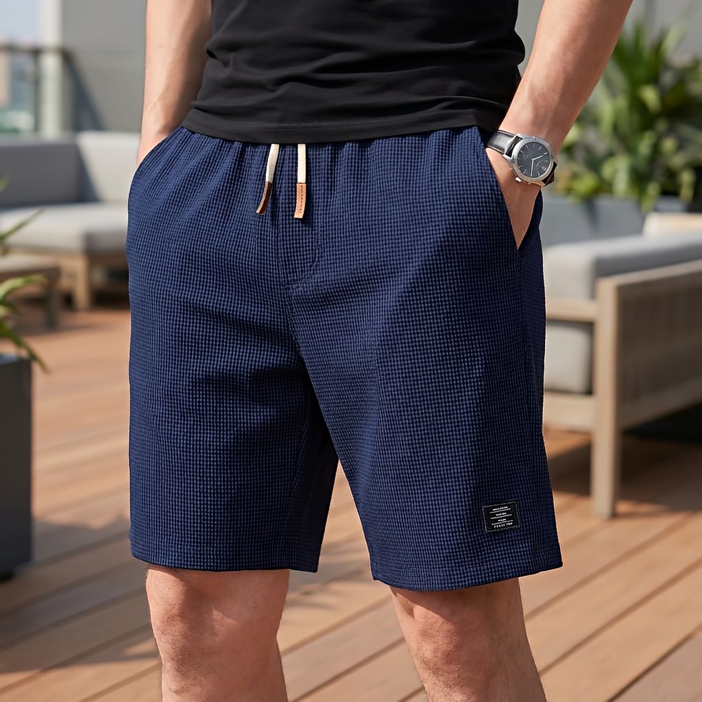 Model wearing navy blue waffle-textured shorts with cream drawstring and leather tips, hand in pocket on a decked terrace 7